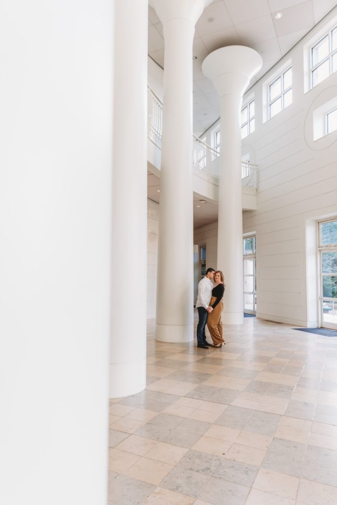 Woman with flowy mustard yellow pants on standing between white columns during her engagement session at Fernbank in Atlanta