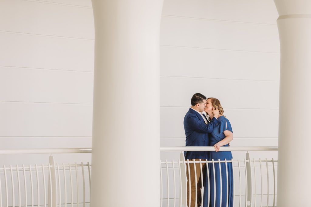 Man and woman wearing blue standing in between white columns during their Fernbank engagement session