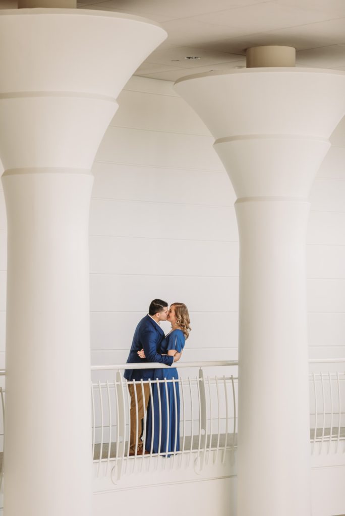 Man and woman wearing blue standing in between white columns during their Fernbank engagement session